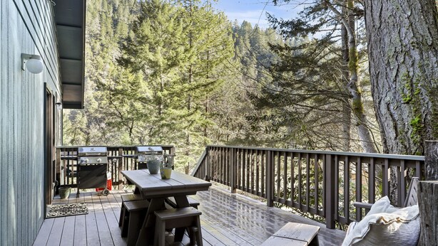 Une terrasse en bois, agrémentée d’une table et de bancs, entourée d’une rambarde et offrant une vue sur une zone boisée.
