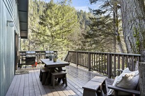 Une terrasse en bois, agrémentée d’une table et de bancs, entourée d’une rambarde et offrant une vue sur une zone boisée.