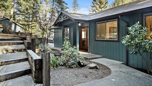 Une cabane avec un escalier en bois menant à une porte, entourée d’un jardin agrémenté de rochers et de plantes.