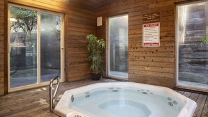 Une salle de spa dotée d’un jacuzzi, de murs en bois, de grandes fenêtres et d’un panneau indiquant les règles à respecter dans le spa.
