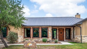 A two-story house with a stone facade, large windows, and a metal roof. - Private pool & hot tub, outdoor kitchen, putting green & more, 5-minute drive to THE Frio River (Concan)