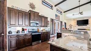 A spacious kitchen with dark wooden cabinets, a granite countertop, and a large island. - Private pool & hot tub, outdoor kitchen, putting green & more, 5-minute drive to THE Frio River (Concan)