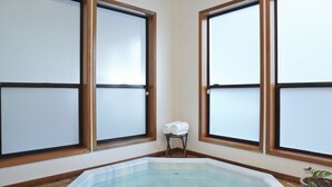 Une pièce dotée d’un jacuzzi entouré de parois en verre, de fenêtres à cadre en bois et d’une petite table avec des serviettes.