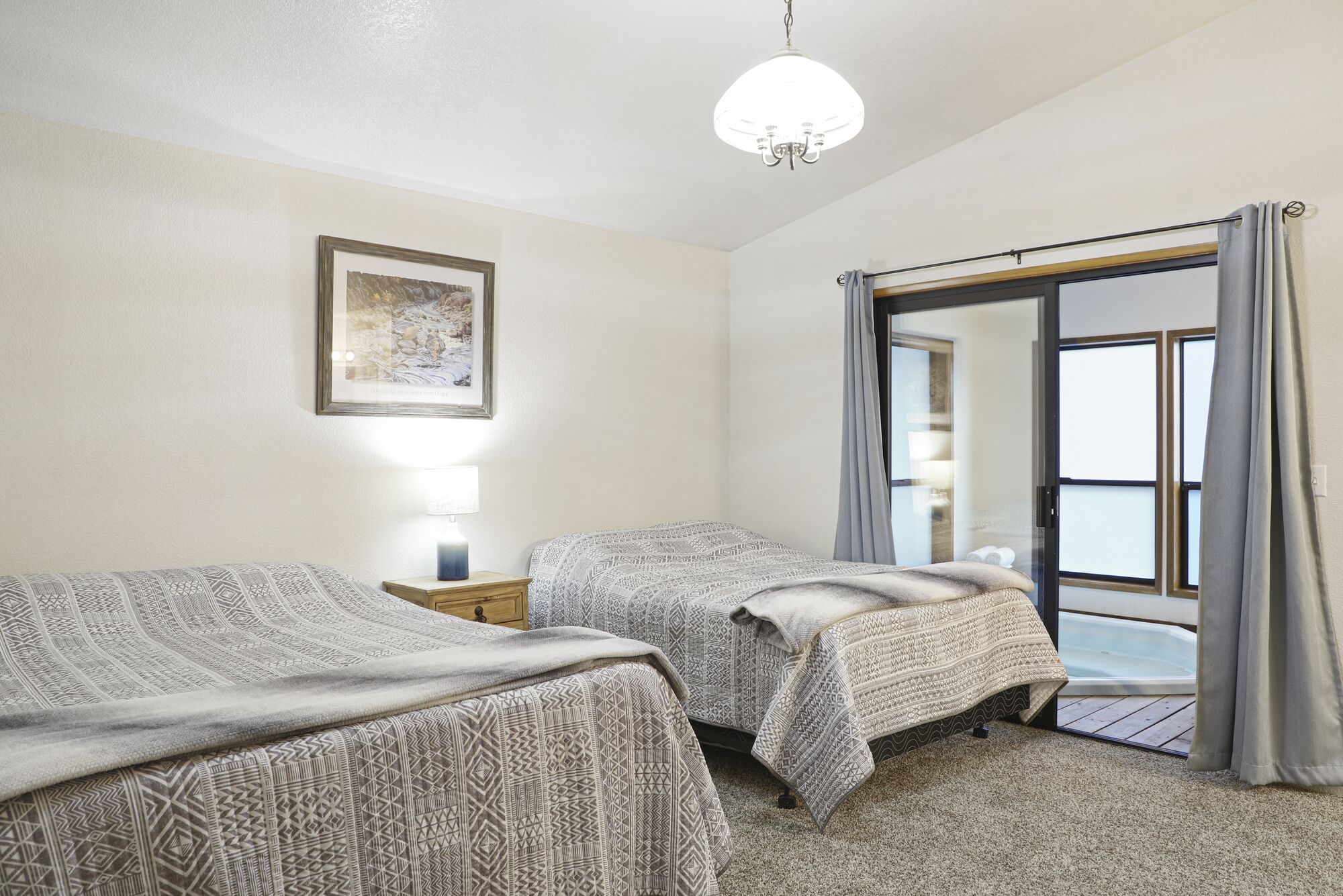 Ein Hotelzimmer mit zwei Betten, einem Nachttisch mit Lampe, einem gerahmten Bild an der Wand und einer Glastür zum Balkon.