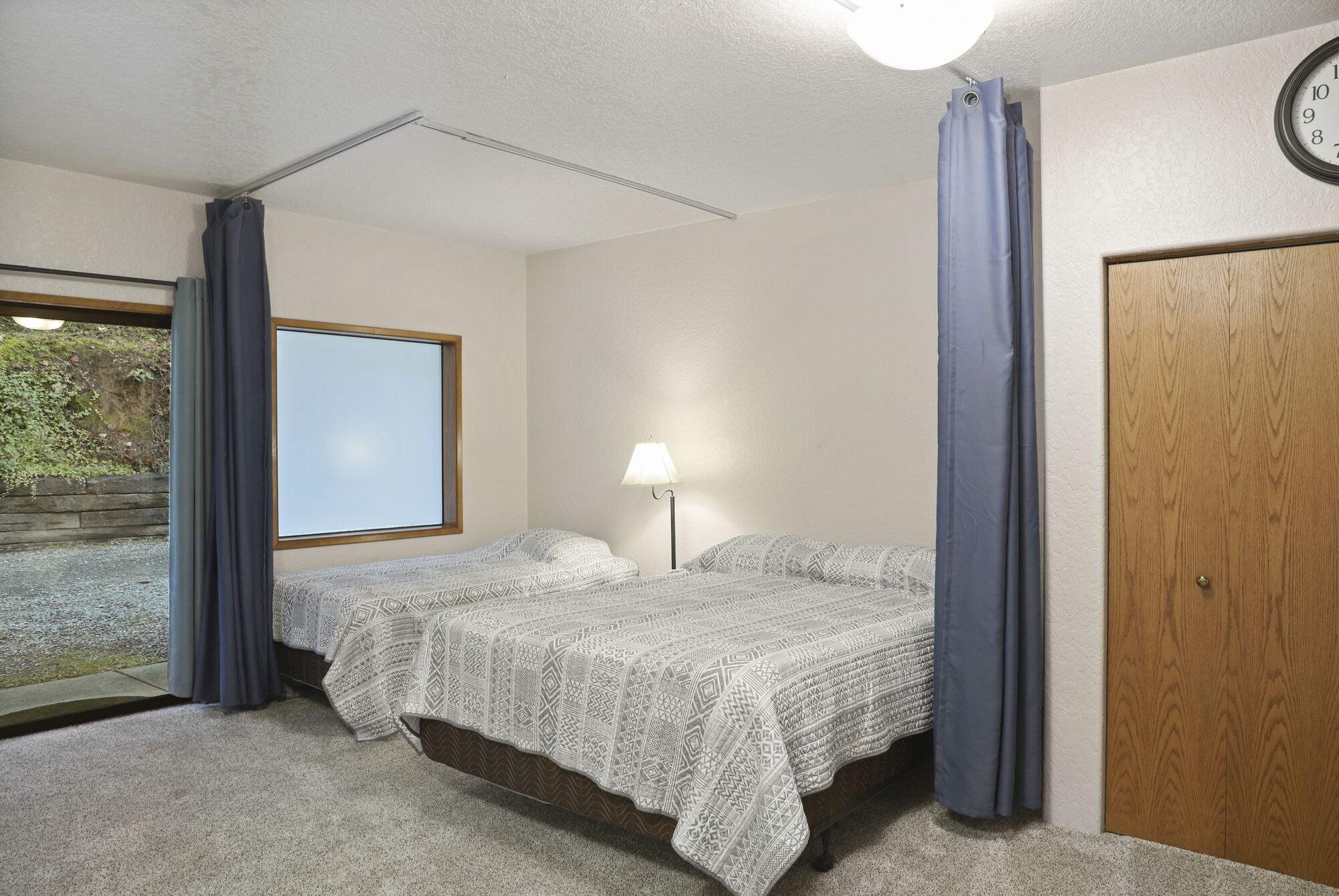 A bedroom with two beds, a window, a lamp, and a door.