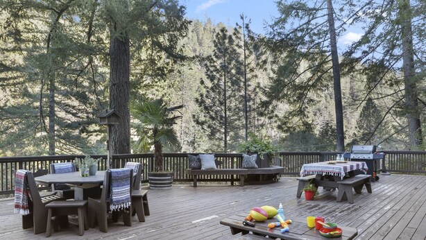 Une terrasse extérieure aménagée avec du mobilier en bois, notamment une table et des bancs, entourée de grands arbres.