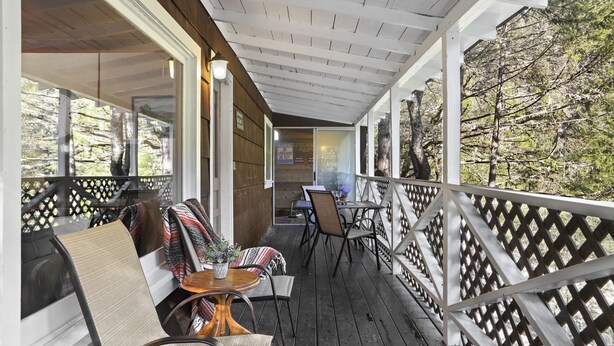 Une véranda couverte avec un plancher en bois, une table avec des chaises et une vue sur les arbres.
