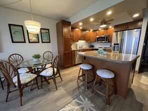 A modern kitchen with wooden cabinets, stainless steel appliances, and a glass dining table with bar stools.