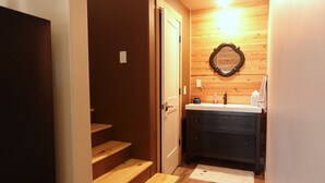 Une salle de bain avec des murs en bois, un miroir, un lavabo et un meuble-lavabo de couleur foncée.