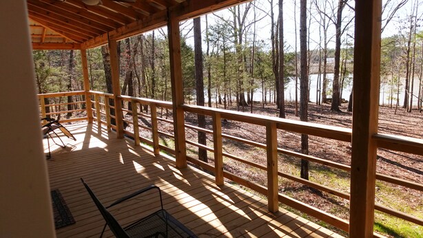 Une terrasse en bois dotée d’une rambarde, offrant une vue sur une zone boisée et un plan d’eau.