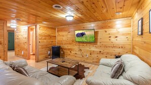 A cozy log cabin interior with a television mounted on the wall, a sofa, a coffee table, and a door leading to another room.