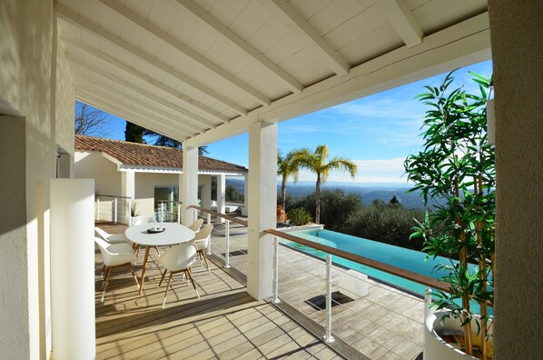 Un espacio al aire libre cubierto con piscina, mobiliario blanco y vistas al paisaje.