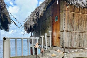 Un edificio de madera con techo de paja, una escalera de concreto y vista al mar.