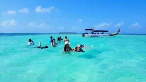 Un grupo de personas haciendo snorkel en aguas turquesas cristalinas, con un barco al fondo.