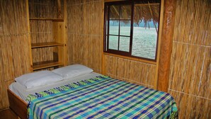 Una habitación con cama, ventana y vistas al mar, y paredes de bambú.