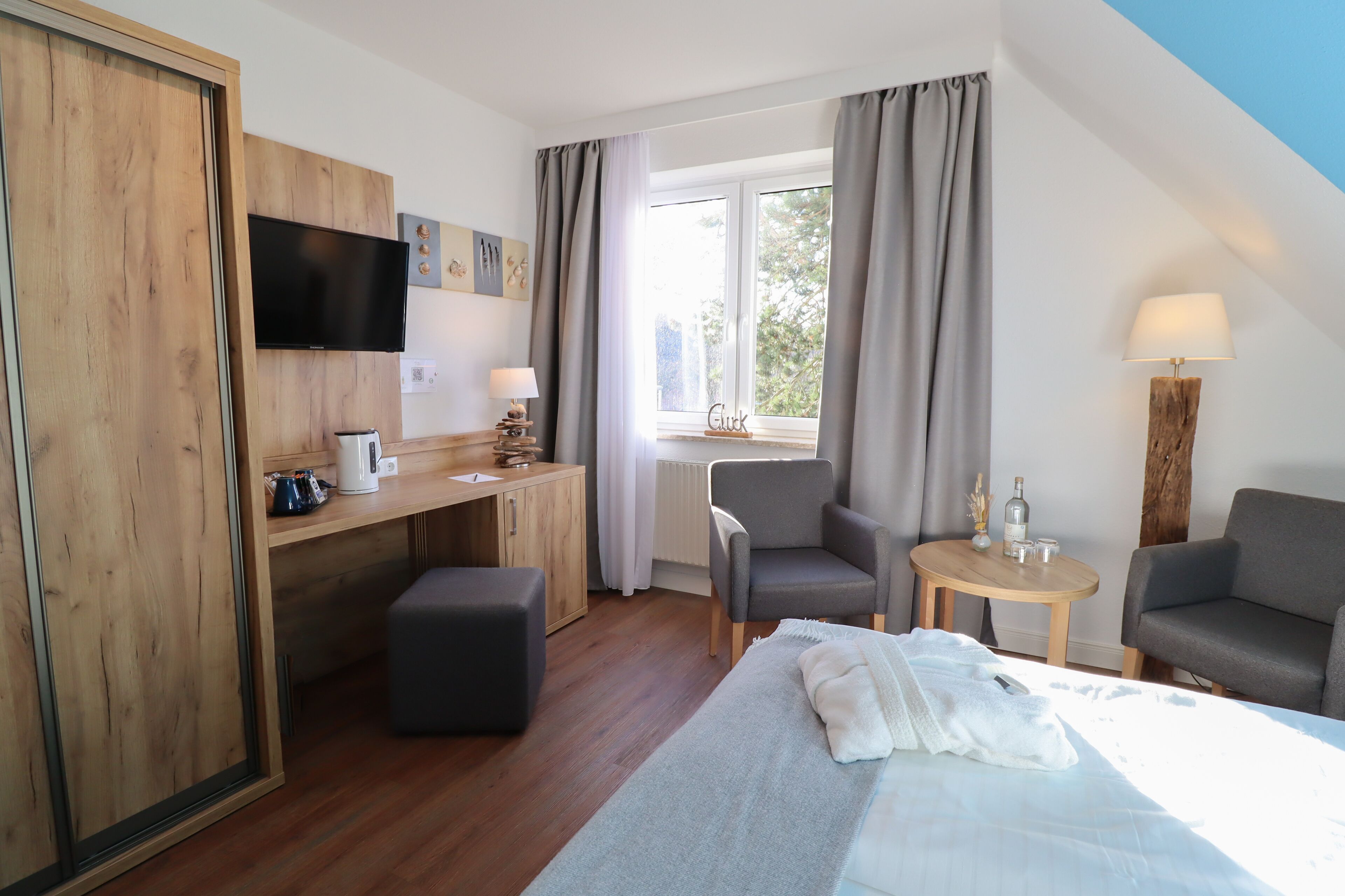 A hotel room with a bed, a desk, a chair, a sofa, a TV, and a window with curtains.