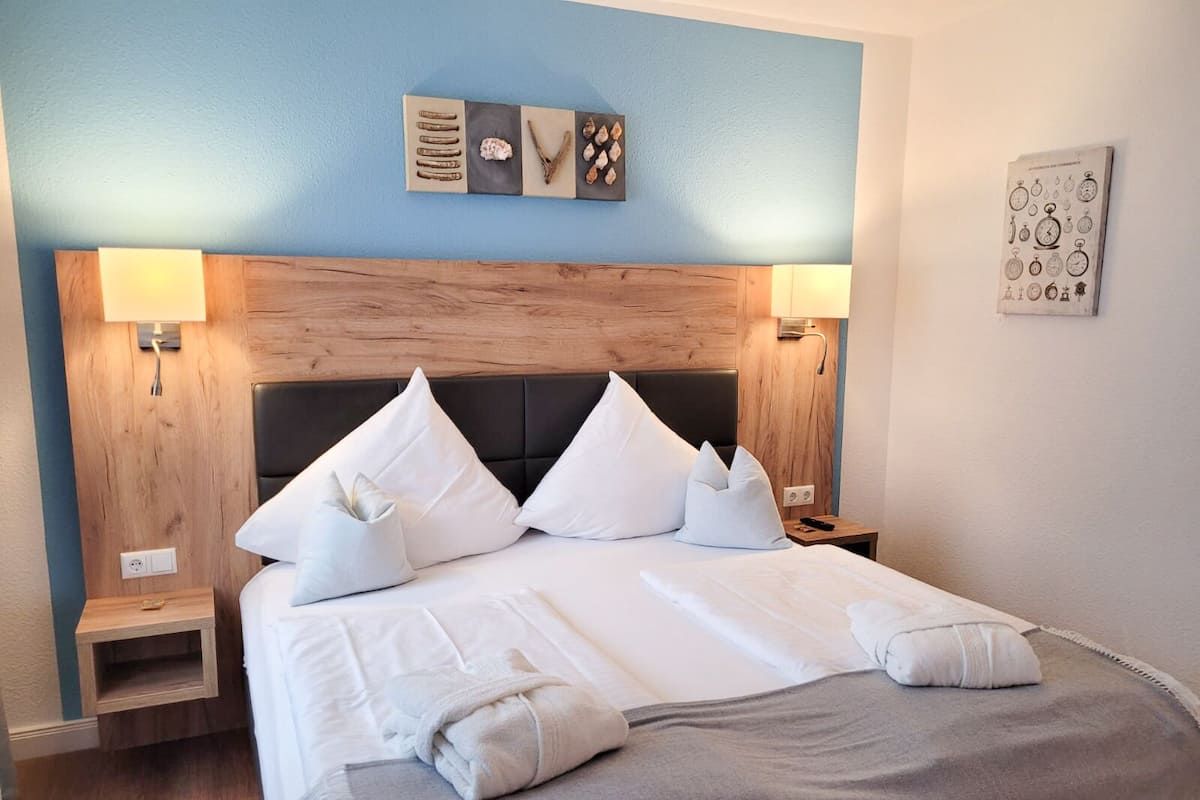 Un lit bien fait, avec du linge de lit blanc et des oreillers, une tête de lit en bois et deux lampes de chevet.