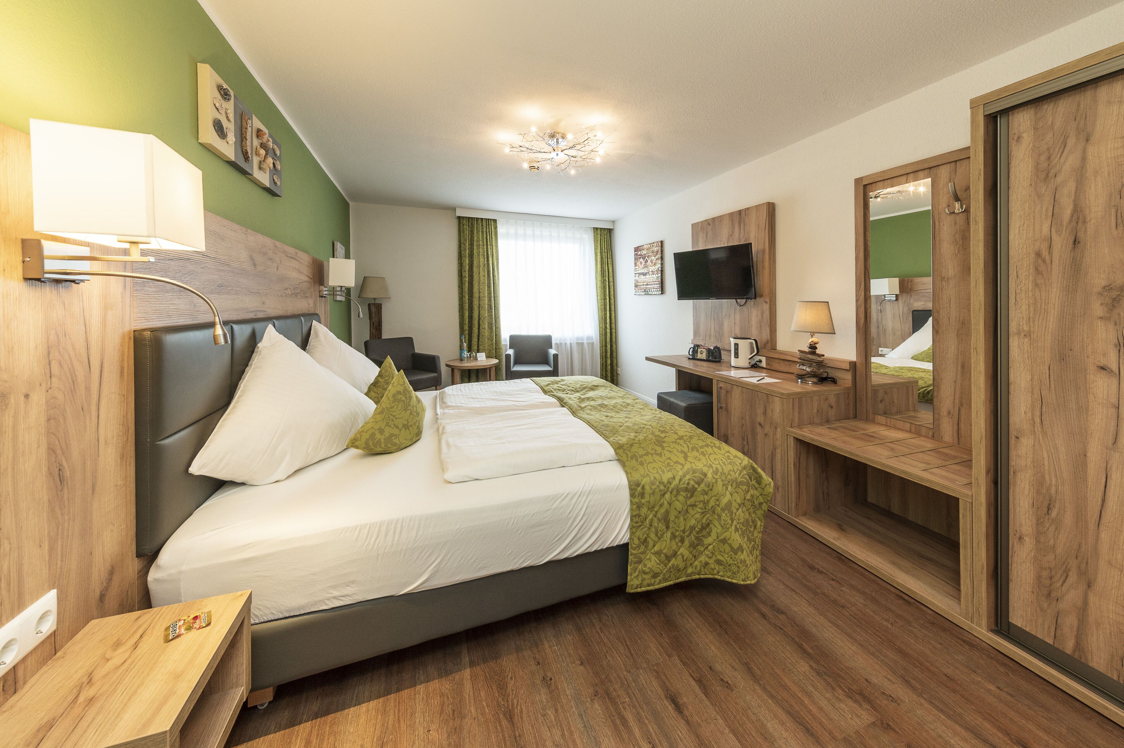 Una camera d'albergo con un letto grande, una scrivania, una sedia, una televisione e uno specchio.