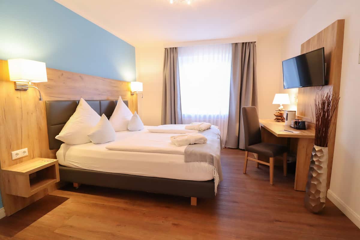 Une chambre d’hôtel comprenant un lit, des tables de chevet, un bureau, une chaise, une télévision et une fenêtre avec des rideaux.