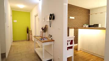 Ein Flur mit grüner Wand, einem Holztisch mit Büchern und einer Vase, einem weißen Stuhl und einer Ziegelwand mit einem weißen Schrank.