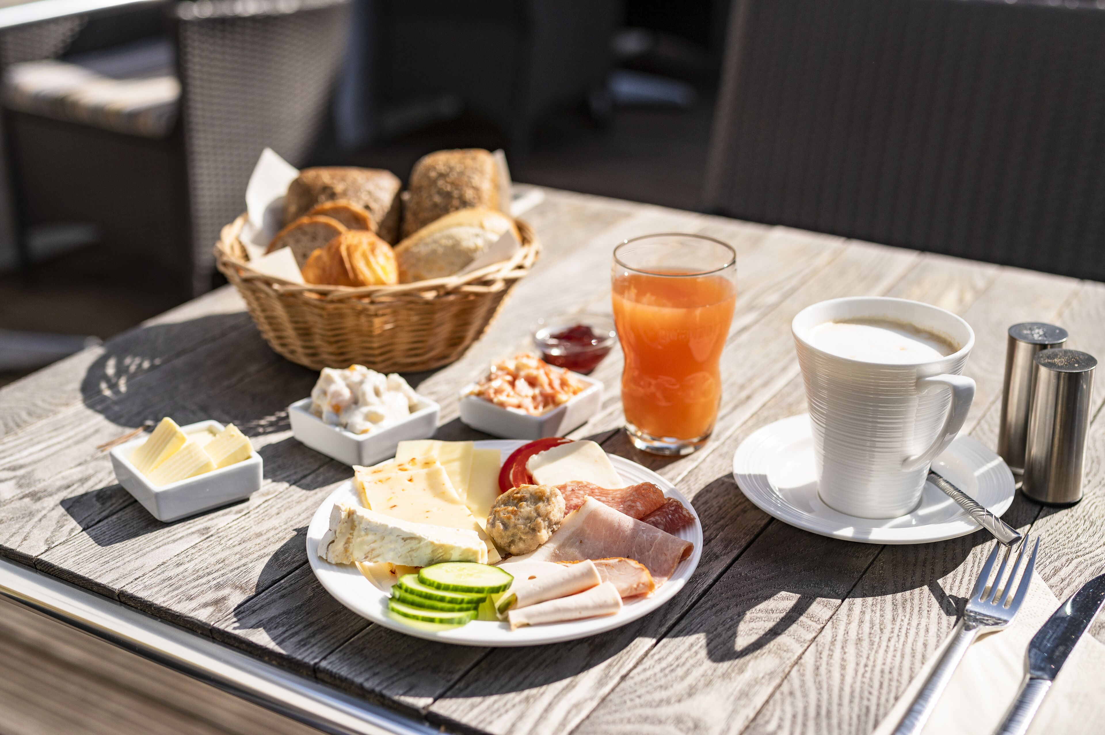 A breakfast table with a variety of foods including bread, cheese, meats, and a glass of orange juice.