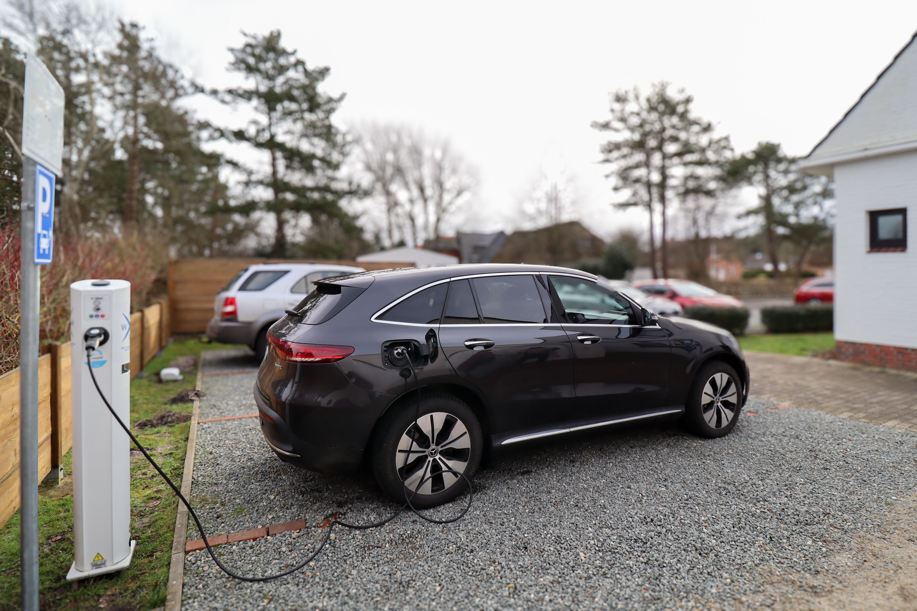 Une voiture noire était garée à une borne de recharge pour véhicules électriques, dans un quartier résidentiel.
