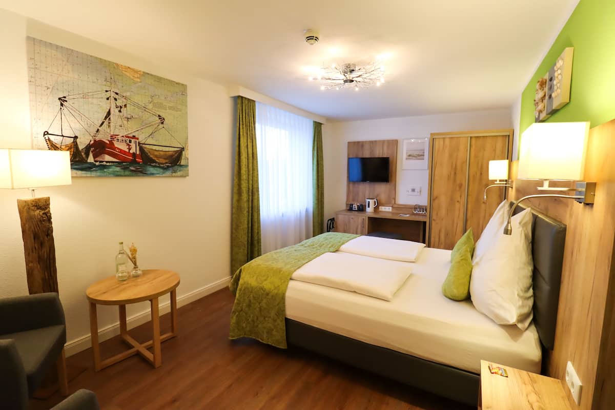 Une chambre d’hôtel comprenant un lit, une petite table, une chaise, un tableau, une télévision et un coin cuisine.