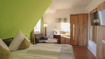 A modern hotel room with a bed, a small table, a chair, a kitchenette, and a TV.