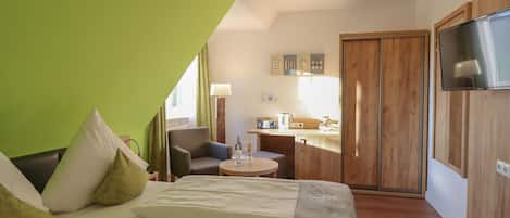 Een moderne hotelkamer met een bed, een tafeltje, een stoel, een kitchenette en een televisie.