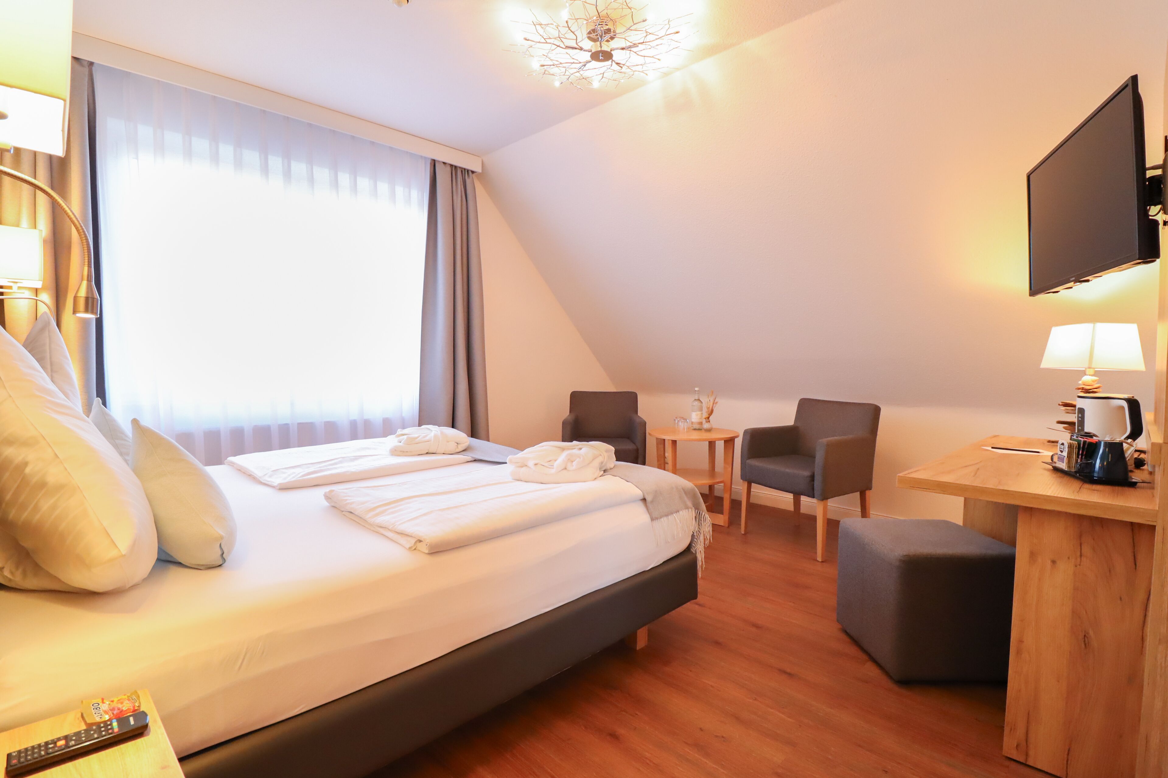 Une chambre d’hôtel avec un grand lit, un bureau avec une lampe, une chaise et un téléviseur fixé au mur.
