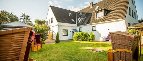 Ein Haus mit geneigtem Dach, einem gepflegten Rasen und Gartenmöbeln.