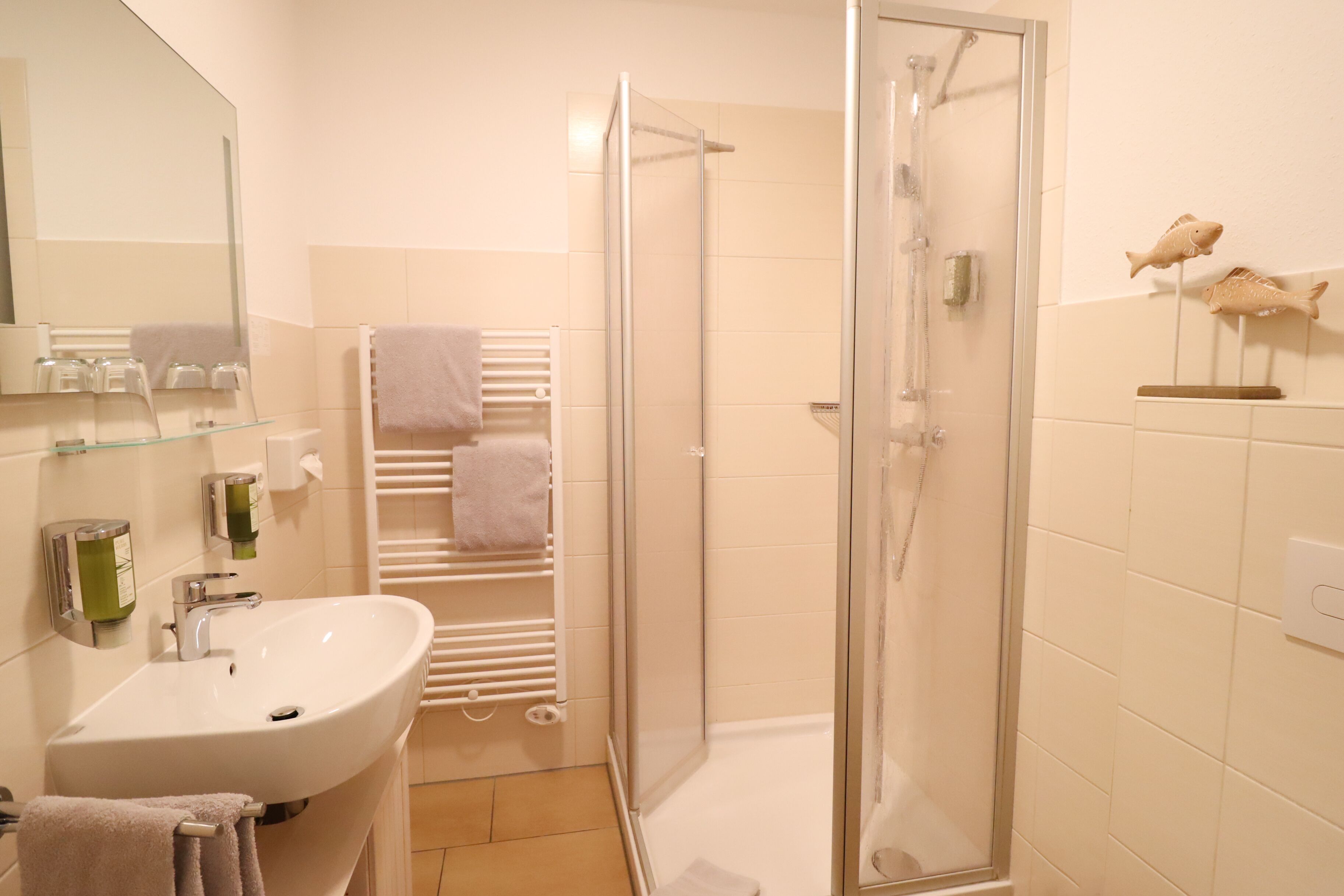 Une salle de bain équipée d’un lavabo, d’un miroir, d’un porte-serviettes, d’une douche et d’un élément décoratif représentant un poisson sur le mur.