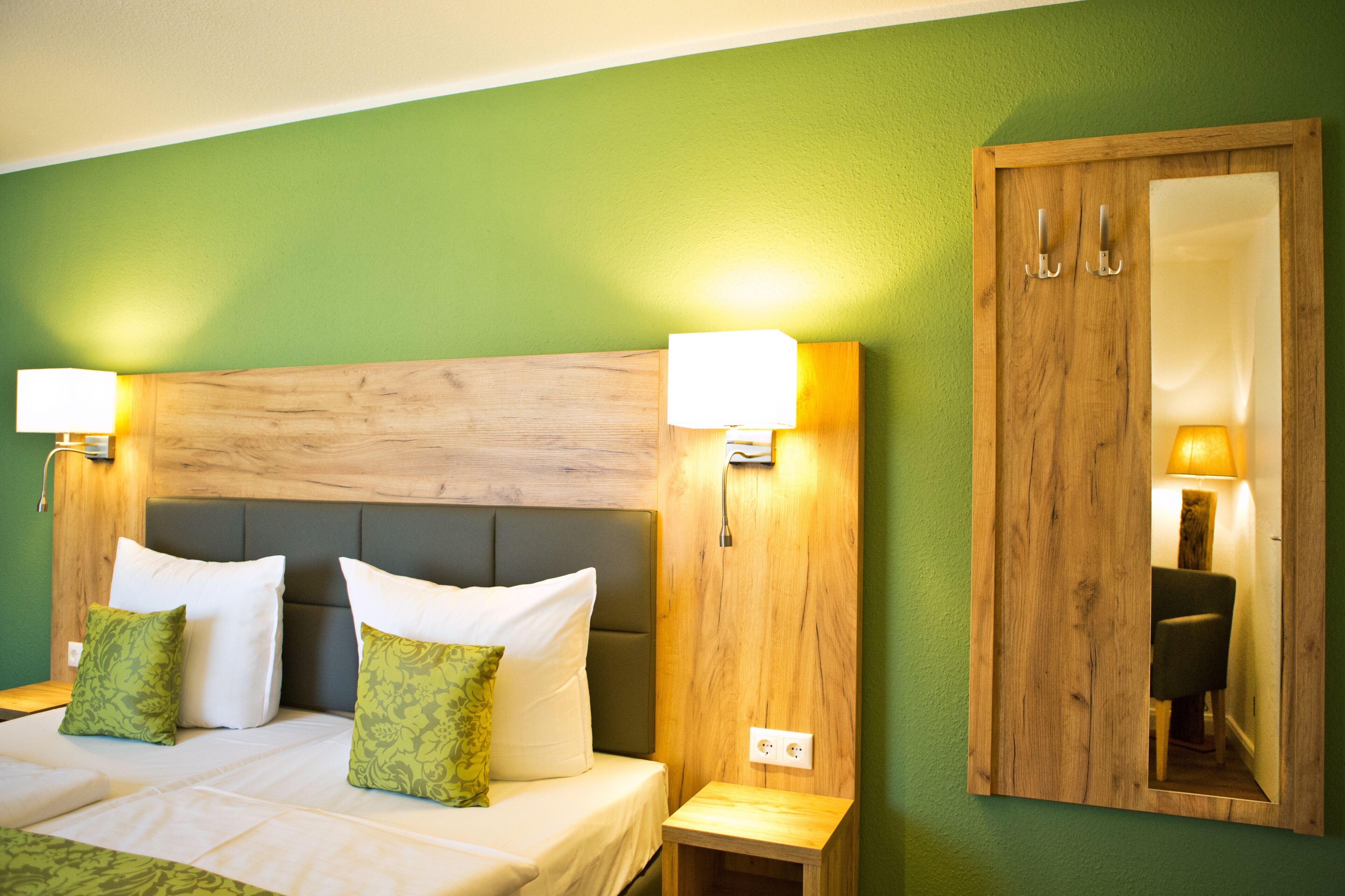 A hotel room with a wooden headboard, two bedside lamps, a mirror cabinet, and green walls.