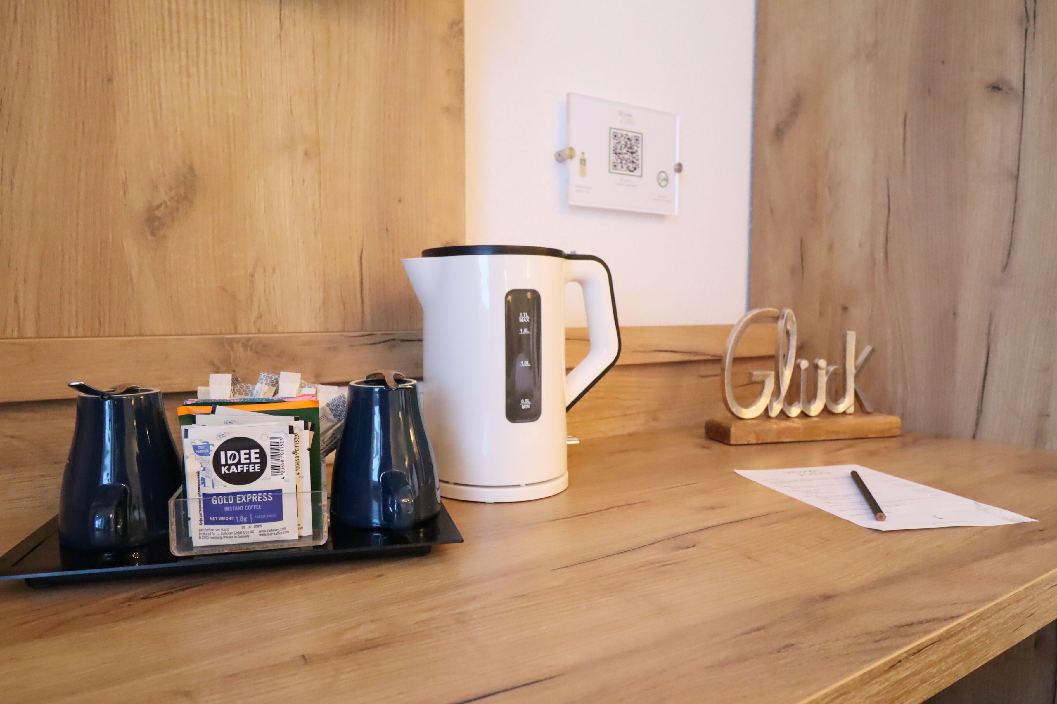 A coffee station with a white coffee maker, a tray with coffee pods, and a wooden sign that reads "Glück".