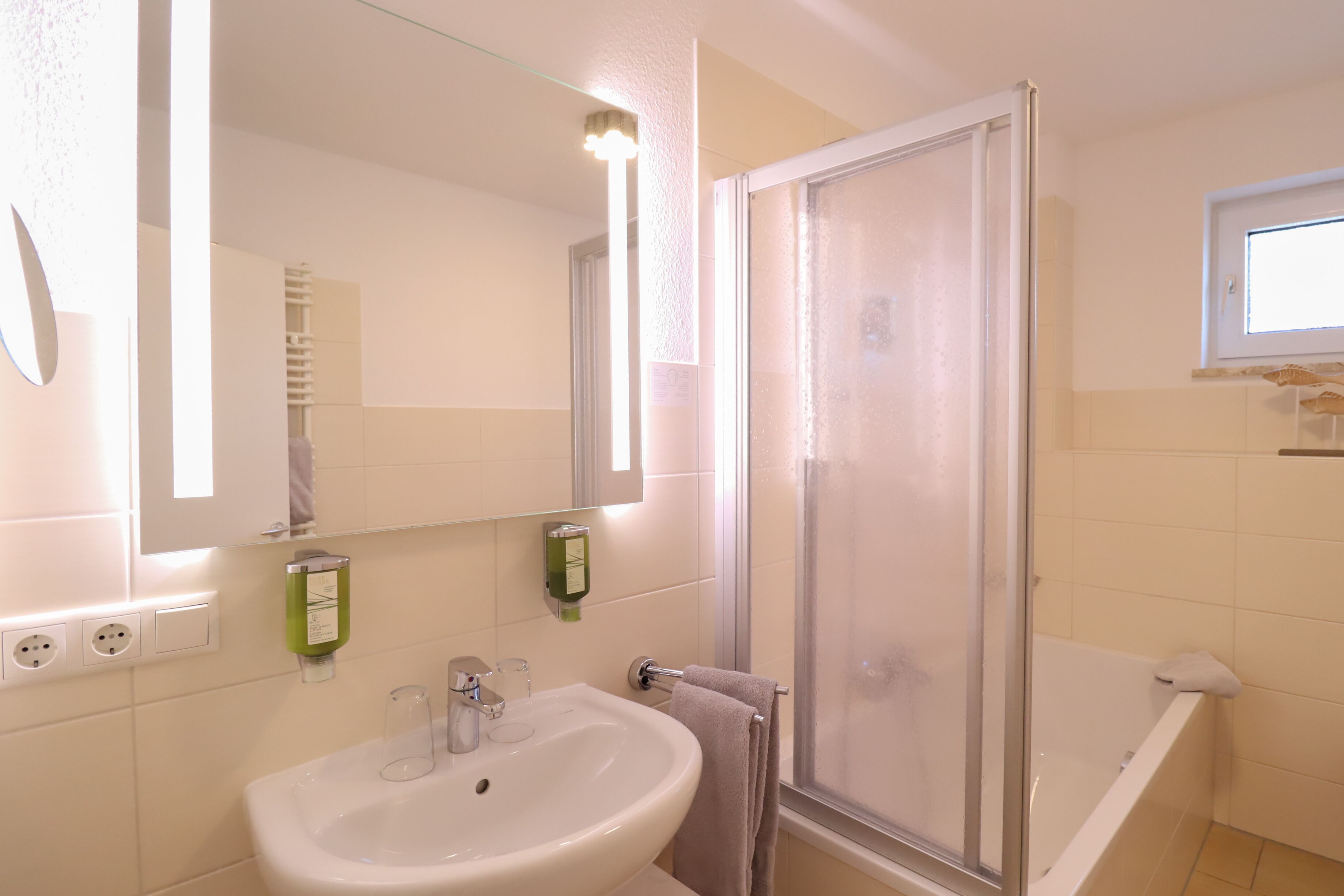 A bathroom with a sink, mirror, towel rack, shower, and a window.