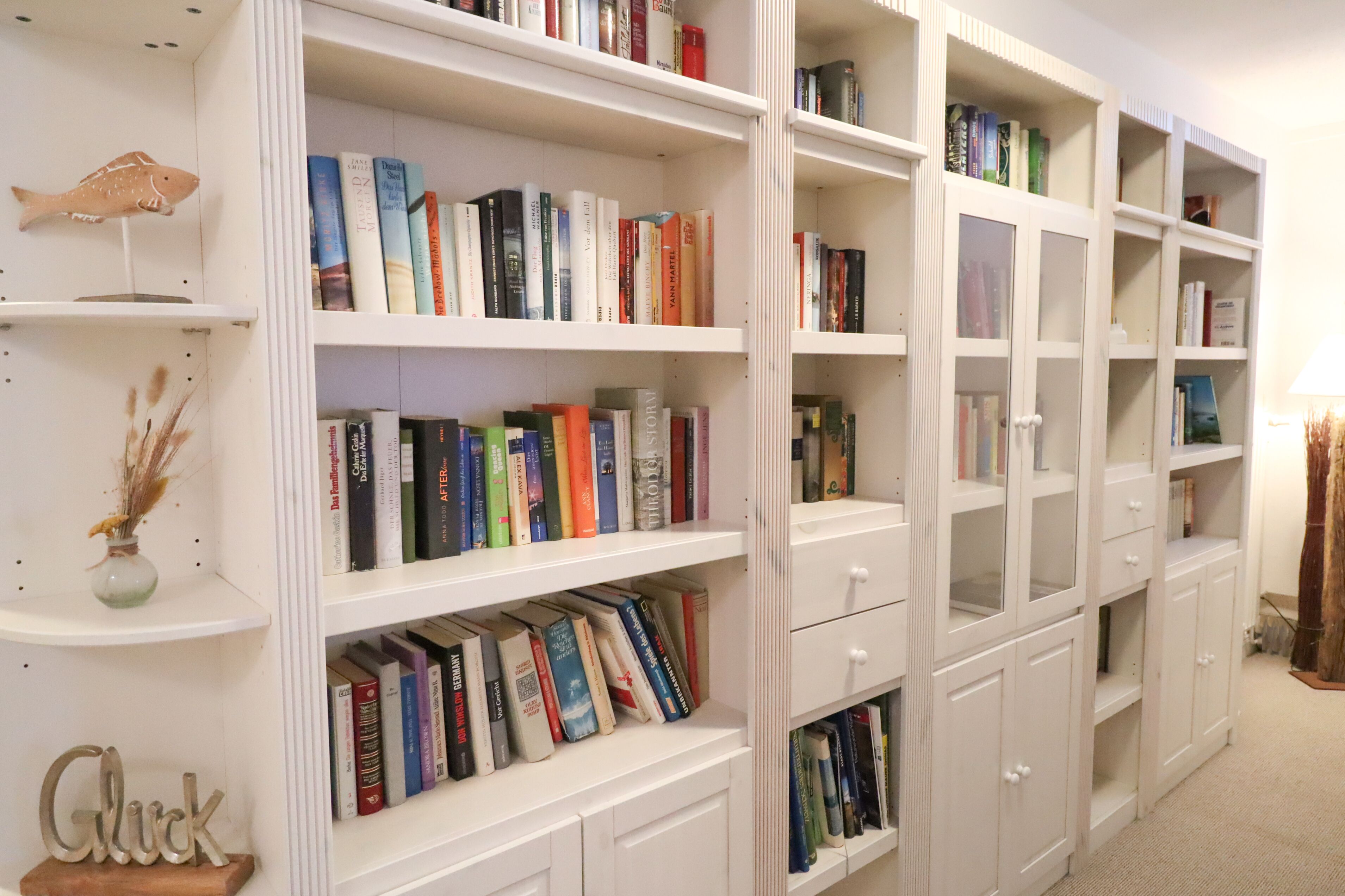 Uma estante cheia de livros, um pequeno peixe decorativo e um letreiro com a palavra 'Glück'.