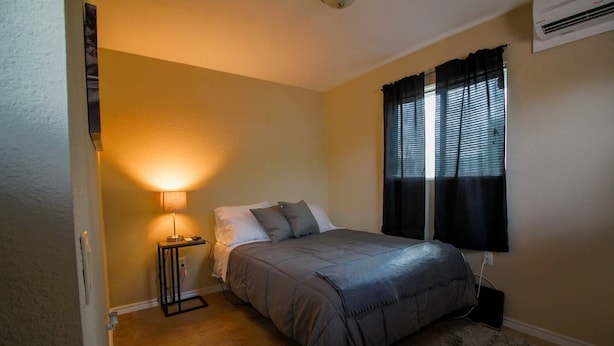 A bedroom with a bed, bedside lamp, and a window with curtains. - Stylish comfortable suite (San Antonio)