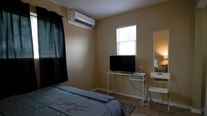 A bedroom with a bed, a desk with a TV, a mirror, and an air conditioning unit. - Stylish comfortable suite (San Antonio)