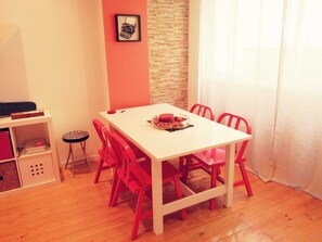 Un coin repas avec une table blanche et des chaises rouges, un petit tabouret et un tableau encadré au mur.