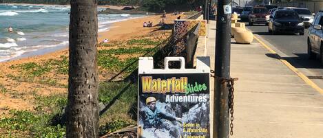 Un cartel en la playa anuncia Waterfall Slides Adventures con información de contacto.