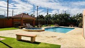 Un patio trasero con piscina, jacuzzi y una zona de estar cubierta con sillones reclinables.