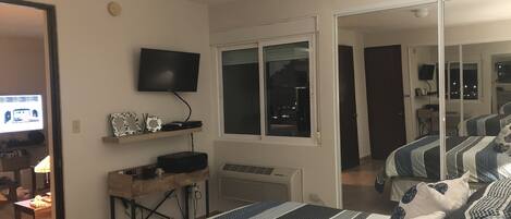 A bedroom with a bed, a TV, a desk, and a window.