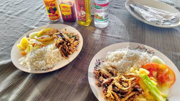 Two plates of food with condiments and a bottle of water on a table.