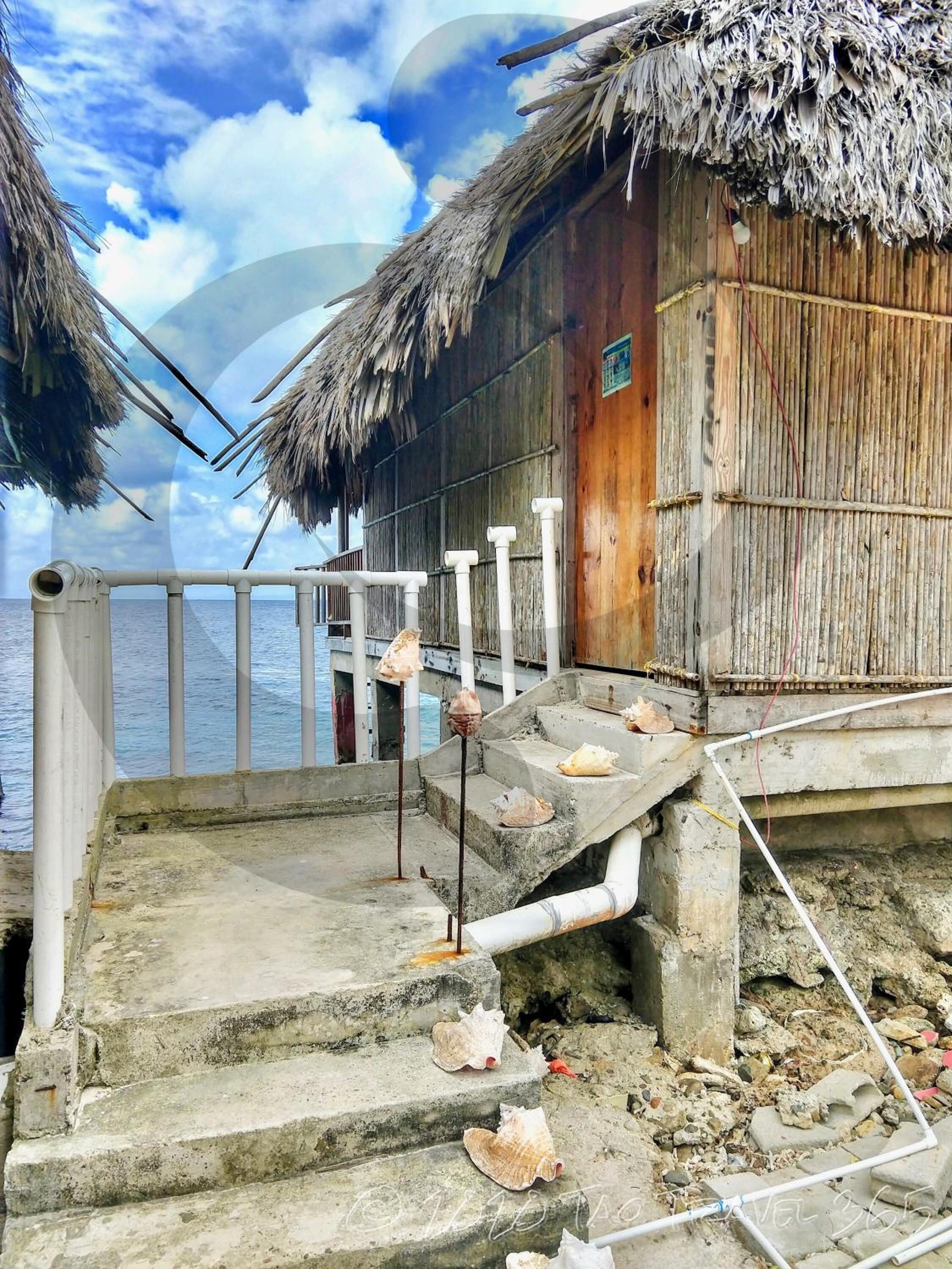 A wooden structure with a thatched roof, concrete steps leading to a wooden door, and a railing along the edge.