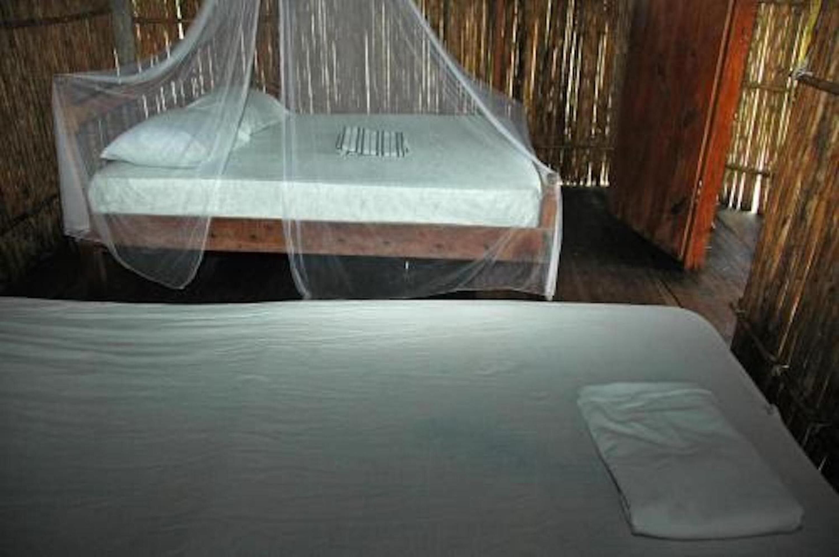A bed with a mosquito net and a mattress in a rustic room with wooden walls.