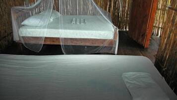 A bed with a mosquito net and a mattress in a rustic room with wooden walls.