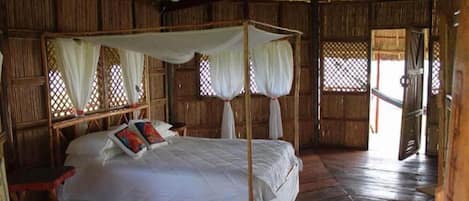 Una habitación con cama con dosel, ropa de cama blanca y ventilador de techo.