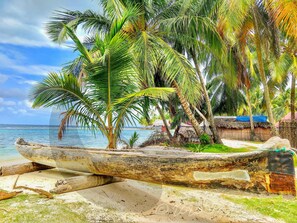 Eine Strandansicht mit einem hölzernen Boot, Palmen und Lehmhütten.