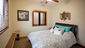 Un dormitorio con cama, ventana con persianas, una obra de arte en la pared y un ventilador de techo.