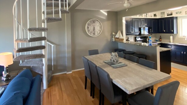 Una cocina moderna con armarios oscuros, una isla central y un comedor con mesa y sillas de madera.